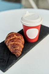 Red cup with coffee and a croissant on a table in a cafe. Morning breakfast. High-quality photo