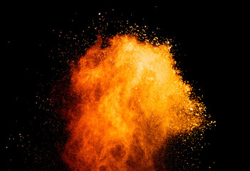 Abstract orange powder explosion. Closeup of orange dust particle splash isolated on black background.