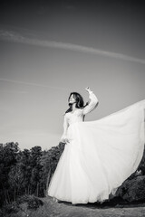 Black and white photo bride in a white dress posing on a hill against the sky.
