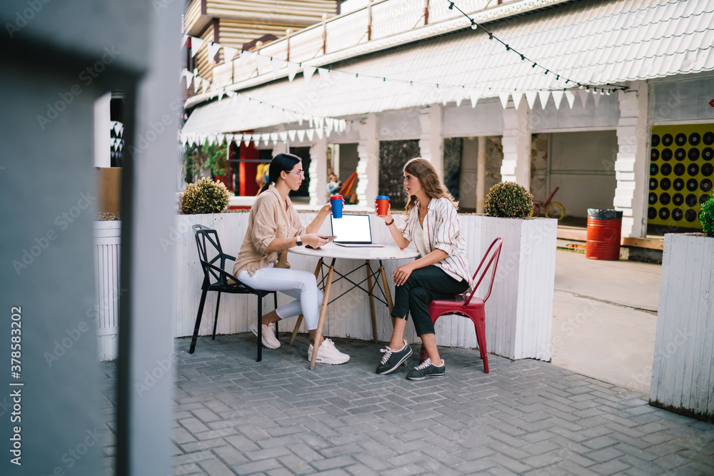 Poster side view of caucasian remote workers sitting at outdoors table and discussing business project for 