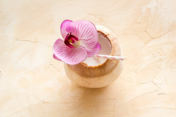 Raw coconut water or milk with straw and orchid flower, above view