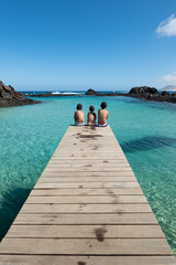 Three children are sitting on the wooden pier in  Isla de Lobos, Canary Islands, Spain.
