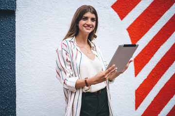 Half length portrait of cheerful hipster blogger 20s standing at urban setting with colorful...