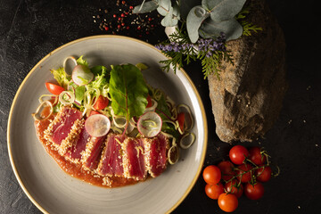 Tuna slices with vegetable salad of cherry tomatoes, radishes, onions, lettuce and adjika tomato sauce. Main fish dish with vegetable garnish