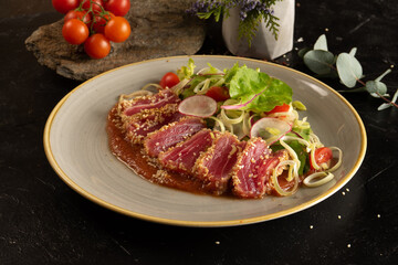 Tuna slices with vegetable salad of cherry tomatoes, radishes, onions, lettuce and adjika tomato sauce. Main fish dish with vegetable garnish