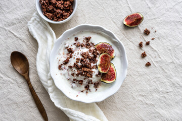 Granola mit Joghurt und frischen Feigen in einer weißen Schüssel. Flat lay, retrostil, beiger Hintergrund.