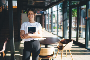 Positive young woman standing with tablet and crossed arm