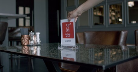 Waitress placing warning sanitizing sign on a table in a restaurant, COVID-19 pandemic, coronavirus spread preventive measures