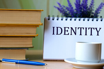IDENTITY - word in a notebook on a background of old books with pen and white cup
