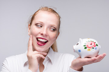 Fototapeta na wymiar Young red haired woman with a piggy bank / porcelain bank is happily smiling
