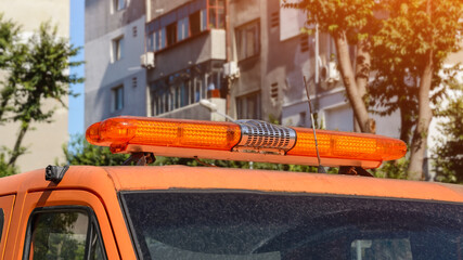 Orange warning lightbar on a stationary car tow track parked on a city street on a summer sunny day. Roof mounted lightbar on a automotive technical assistance vehicle.