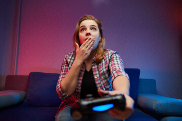 Portrait of crazy playful Gamer, girl enjoying Playing Video Games indoors sitting on the sofa, holding Console Gamepad in hands. Resting At Home, have a great Weekend