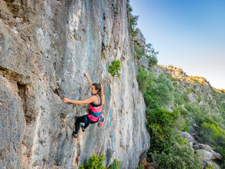 A woman in harness climbing a steep rock