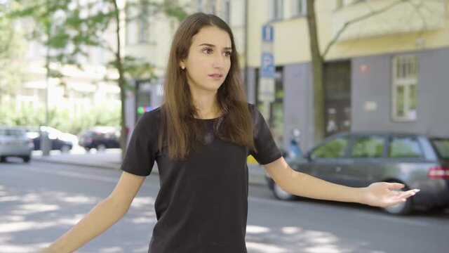 A young Turkish woman acts frustrated and at a loss in the street in an urban area  - a road with cars and a building in the blurry background