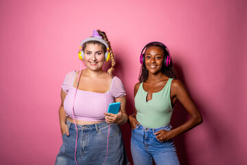 Fit and oversize young adull posing on pink background listening music - Diverse women with different body shapes isolated on background