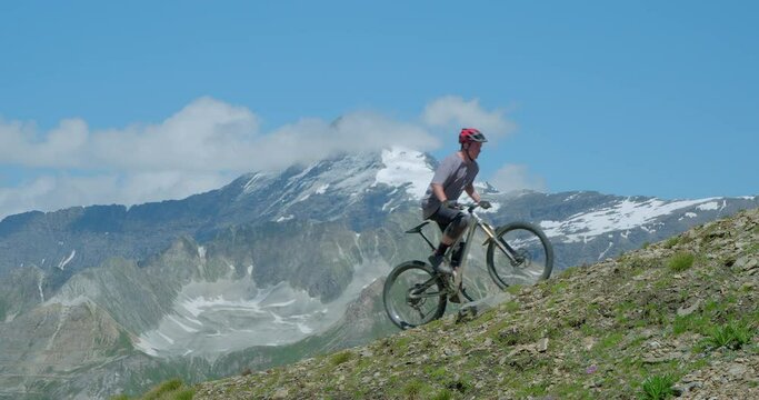Two Mountain Bikers peddling fast and hard up a steep mountain side with glaciers and peaks.