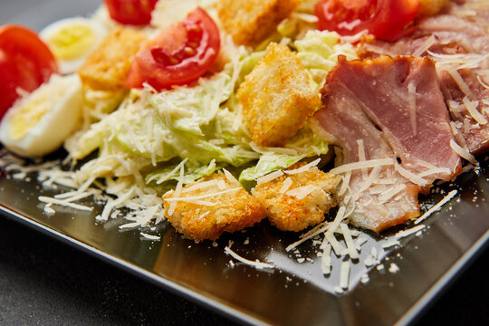 Caesar salad with lettuce, chicken, bacon and croutons on dark background