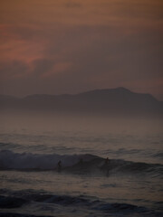 Person bathing and people surfing during sunset in Zumaia.