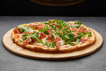 Delicious Italian Pizza with Parma ham and arugula, mozzarella cheese on dark background