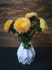 Callistephus chinensis, Asters in pleated white ceramic vase on dark surface, old weathered wooden boards  background, seasonal  decorating ideas, bold gold orange yellow color