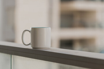 Close-up view of white blue coffee cup on sky terrace border on balcony with blurred morning city scape background. Selective focus and copy space. Beverage, breakfast. Hot tea in the mug. Morning.