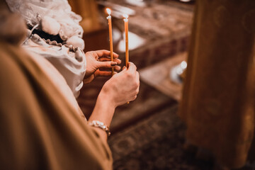 Female hands hold two burning candles in the church.