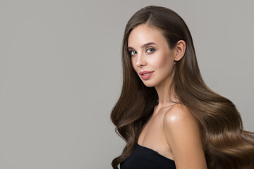 Portrait of young smiling brunette woman with makeup and hairstyle. Shiny wavy hair on gray...