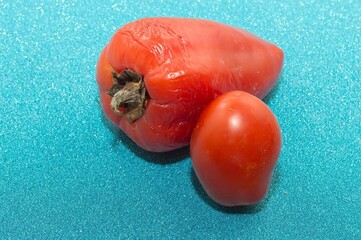 Wilting red vegetables: peppers and tomatoes on a shiny blue surface.