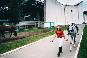 Female horsewoman in riding boots walking with horse along street