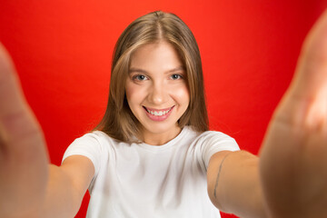 Selfie view. Portrait of young caucasian woman on red studio background with copyspace. Blonde female model. Concept of human emotions, facial expression, sales, advertising, youth.