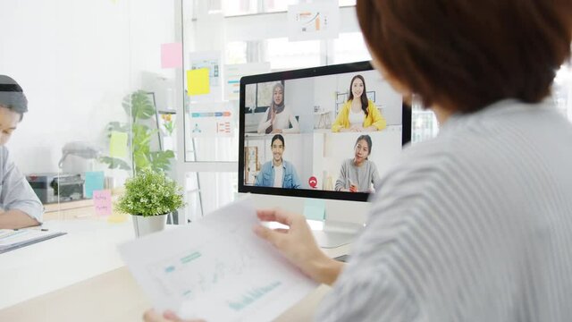 Asia businesspeople using desktop talk to colleagues discussing business brainstorm about plan in video call meeting in new normal office. Lifestyle social distancing and work after corona virus.