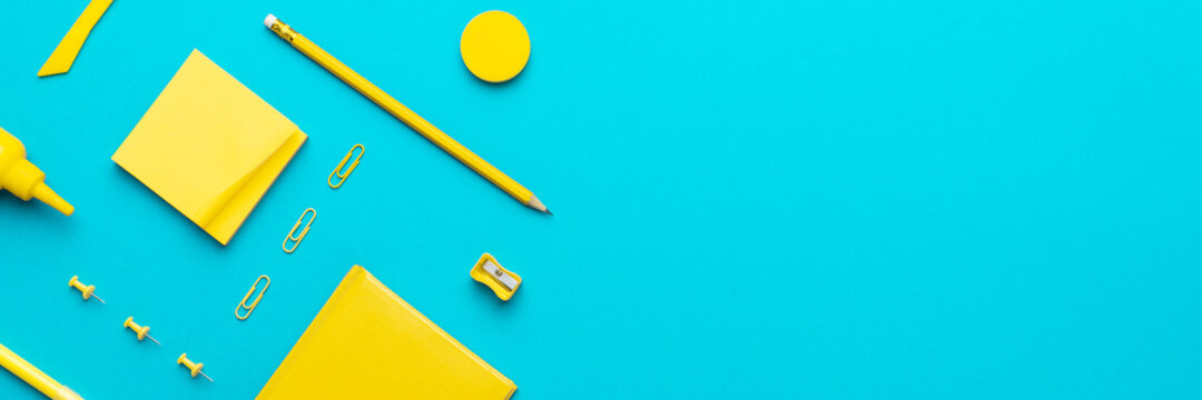 Top view photo of yellow stationery over turquoise blue background with copy space. Flat lay image of different stationary objects as back to school background.