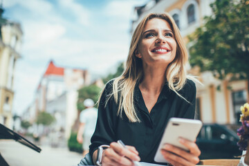 Cheerful female with cute smile on face holding cellular device for browser networking enjoying...