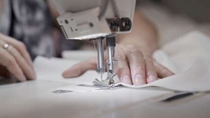 Sewing white cloth on a white sewing machine close up. Concept of sewing in modern bright studio,...