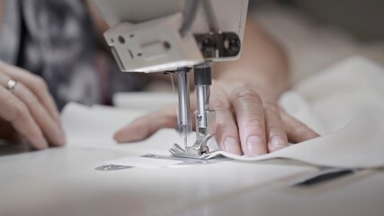 Sewing white cloth on a white sewing machine close up. Concept of sewing in modern bright studio, female hands sewing a white cloth, selective focus