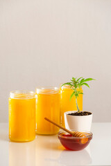 Three jars of CBD honey, a marijuana plant and honey in a bowl