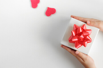 Composition with a gift box in children's hands and hearts. Top view, gray background. Place for...