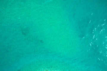 Turquoise Water near to the Sand underneath forming many little waves reflecting the sun. Turquoise water top view.