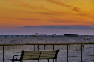 Fototapeta na wymiar Red Sunset, over Ocean Beach Board Walk. High quality photo, with Red Clouds, Beach Bench, Birds