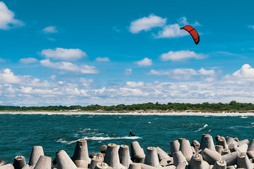 Kite surfer in the sea on the waves with a red sail against a blue cloudy sky.
