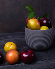 Colorful plums fruit in pot and plate on the dark background top view