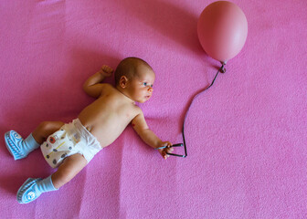 newborn baby lies on a pink background with a balloon