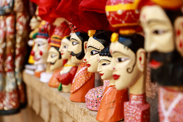 Colorful human face shaped Puppets wearing colorful clothes hanging against the wall in Rajasthan...