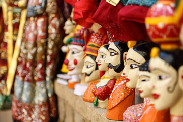 Colorful human face shaped Puppets wearing colorful clothes hanging against the wall in Rajasthan...