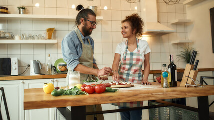 The perfect chef. Young couple making pizza together at home. Man in apron adding mozzarella cheese on the dough while woman looking at him. Hobby, lifestyle