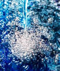 Bluish fresh water splashes and forms air bubbles and jumping water drops on a blue background