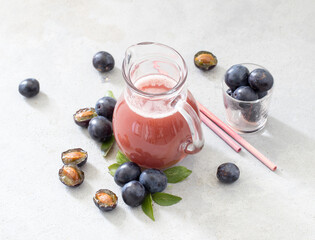 Juice fruit of black plums in a glass jug on a light gray background top view