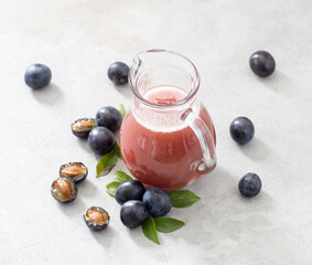 Juice fruit of black plums in a glass jug on a light gray background top view