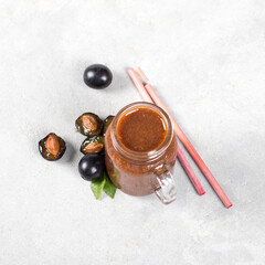 Plum smoothie in a glass jar with bamboo straws on a light gray background top view