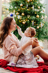 Obraz premium mother and little daughter sitting at the Christmas tree. happy motherhood. new year. family holidays. maternal love